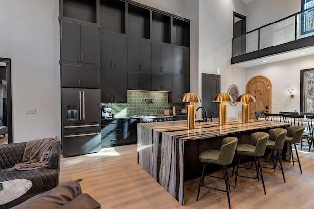 kitchen featuring a high ceiling, stainless steel appliances, light hardwood / wood-style flooring, and decorative backsplash