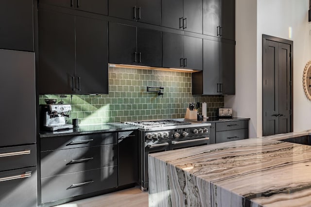 kitchen featuring high quality appliances, dark stone countertops, light hardwood / wood-style flooring, and tasteful backsplash