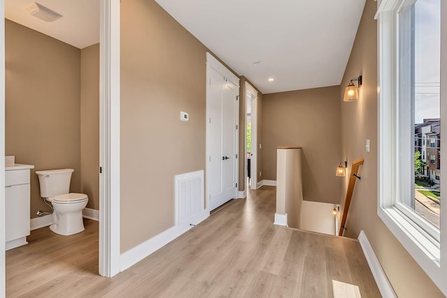 hallway with an upstairs landing, visible vents, a wealth of natural light, and light wood-style floors