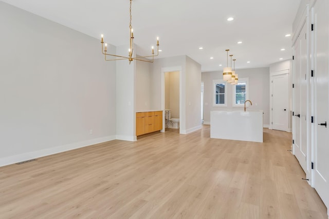 interior space featuring a kitchen island with sink, sink, pendant lighting, light hardwood / wood-style flooring, and an inviting chandelier