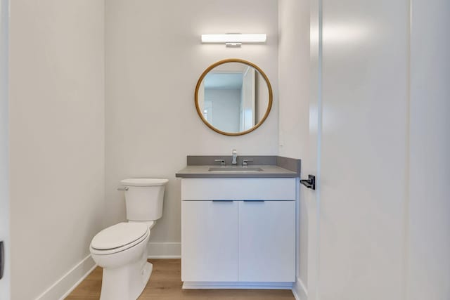 half bath with vanity, toilet, wood finished floors, and baseboards