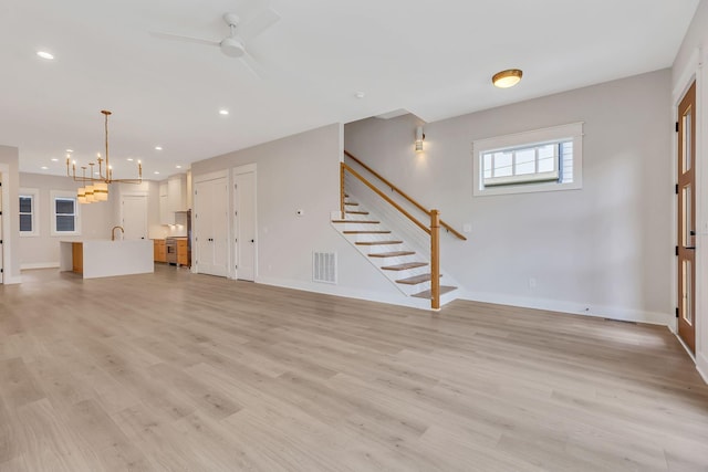 unfurnished living room with ceiling fan with notable chandelier, light hardwood / wood-style flooring, and sink