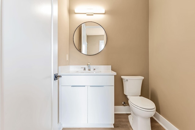 half bath featuring baseboards, toilet, wood finished floors, and vanity