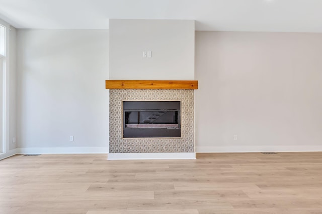 unfurnished living room with a tiled fireplace and light hardwood / wood-style flooring