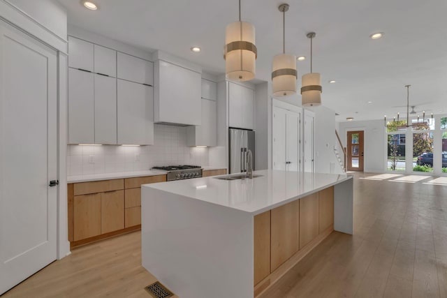 kitchen with a kitchen island with sink, white cabinets, sink, hanging light fixtures, and decorative backsplash