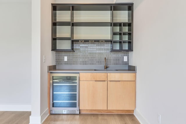 bar with beverage cooler, backsplash, light wood-style floors, and a sink