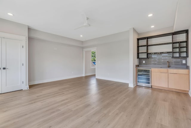 bar with beverage cooler, backsplash, light wood-type flooring, and a ceiling fan