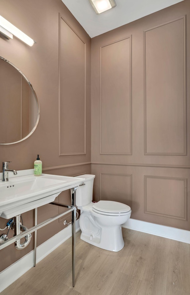 half bathroom featuring toilet, wood finished floors, and a decorative wall