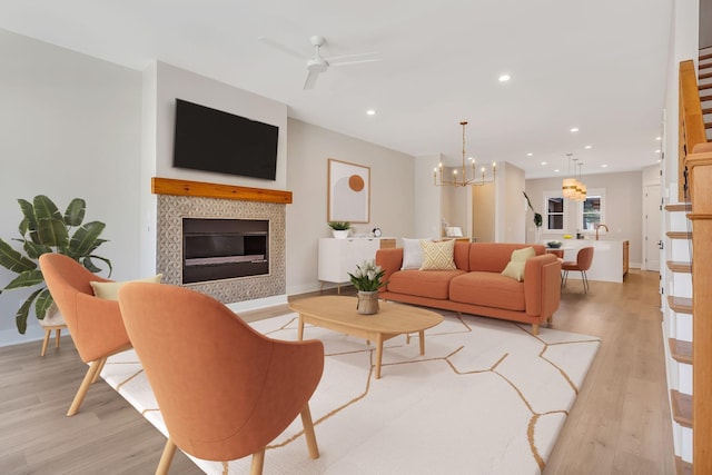 living area featuring a tiled fireplace, recessed lighting, ceiling fan with notable chandelier, and light wood-type flooring