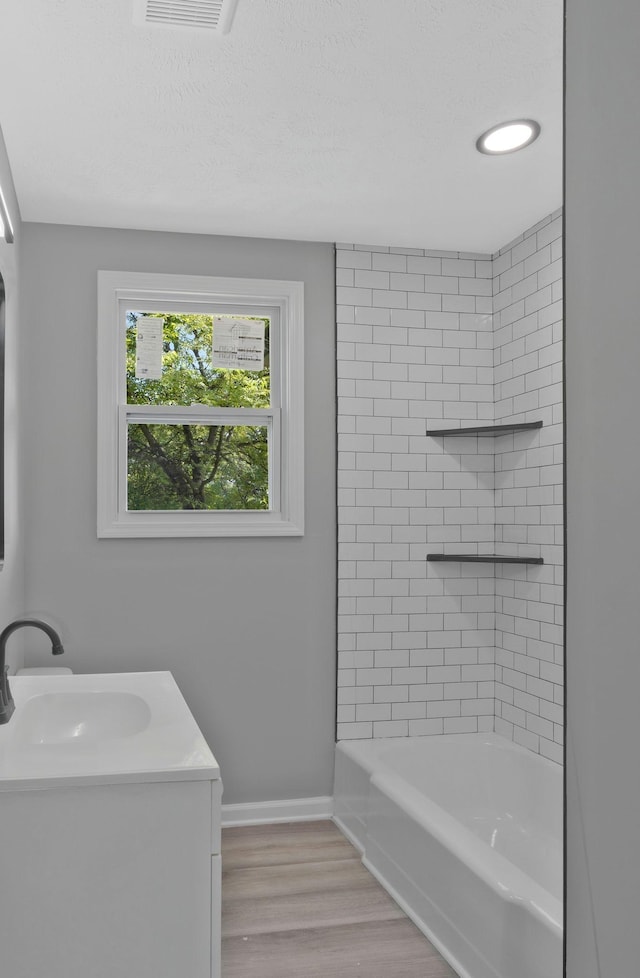 bathroom with hardwood / wood-style flooring, vanity, a textured ceiling, and tiled shower / bath