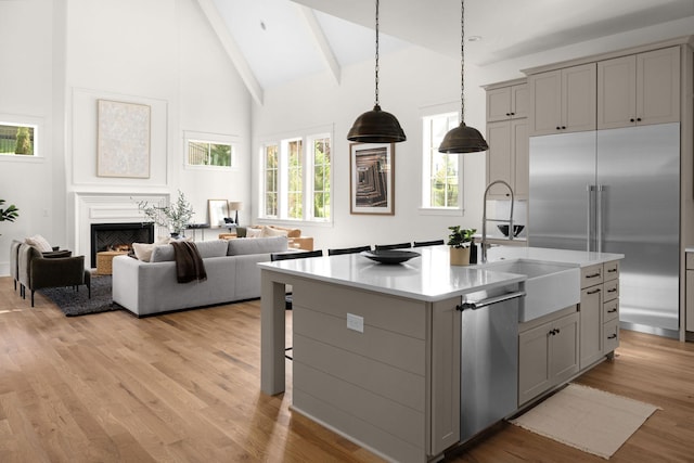 kitchen featuring gray cabinets, beamed ceiling, an island with sink, and appliances with stainless steel finishes