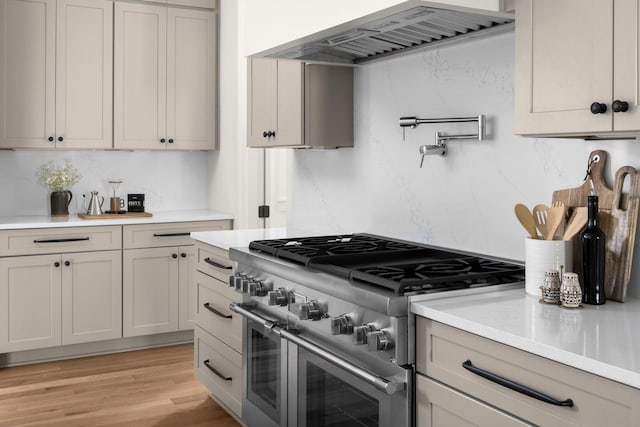 kitchen with decorative backsplash, light hardwood / wood-style floors, double oven range, and wall chimney range hood