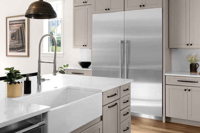 kitchen featuring light wood-type flooring, backsplash, sink, pendant lighting, and stainless steel built in fridge