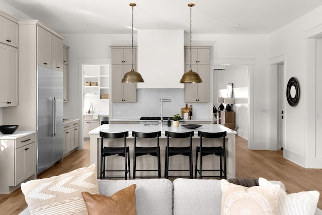 kitchen with hanging light fixtures, light hardwood / wood-style flooring, stainless steel built in refrigerator, a breakfast bar area, and a kitchen island with sink