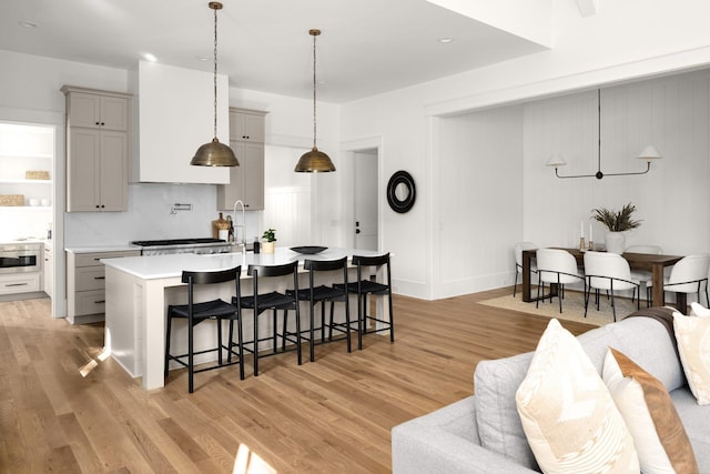 kitchen featuring gray cabinetry, a kitchen breakfast bar, an island with sink, decorative light fixtures, and light hardwood / wood-style floors