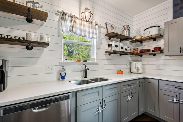 kitchen with stainless steel dishwasher, wooden walls, sink, gray cabinets, and hanging light fixtures