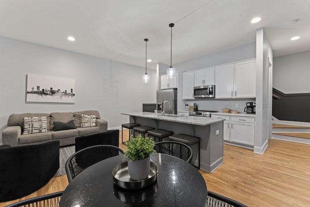 kitchen with a kitchen island with sink, hanging light fixtures, light stone countertops, white cabinetry, and stainless steel appliances