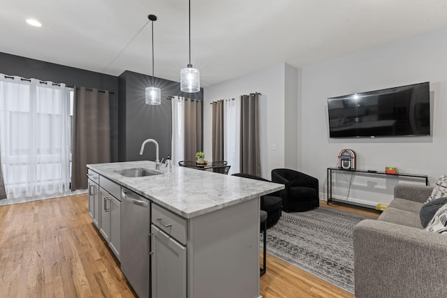 kitchen featuring sink, hanging light fixtures, light stone counters, stainless steel dishwasher, and a center island with sink