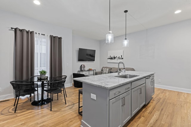 kitchen with stainless steel dishwasher, a kitchen island with sink, sink, gray cabinets, and hanging light fixtures