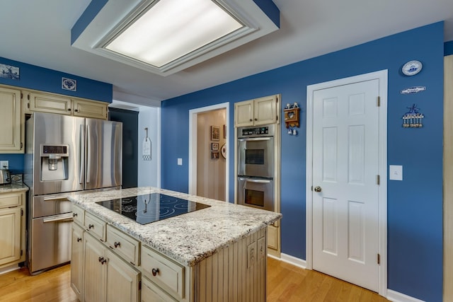 kitchen featuring a center island, light hardwood / wood-style flooring, appliances with stainless steel finishes, light stone countertops, and cream cabinets