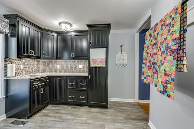 kitchen with light stone counters, sink, decorative backsplash, and light hardwood / wood-style floors