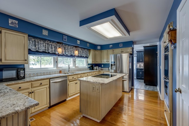 kitchen featuring sink, light hardwood / wood-style flooring, light stone counters, black appliances, and a kitchen island