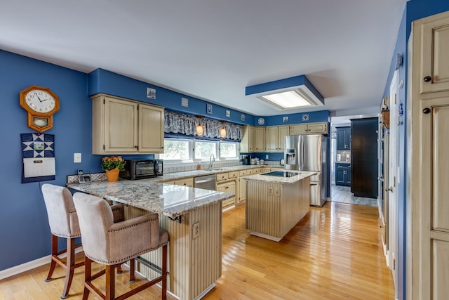 kitchen with light hardwood / wood-style flooring, a center island, black appliances, a kitchen bar, and kitchen peninsula