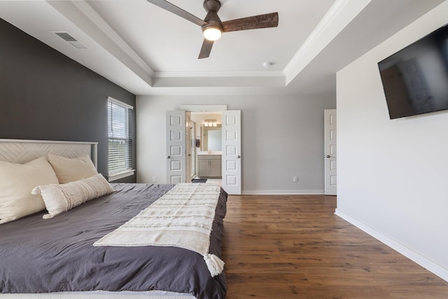 bedroom with a tray ceiling, ceiling fan, crown molding, connected bathroom, and dark hardwood / wood-style floors