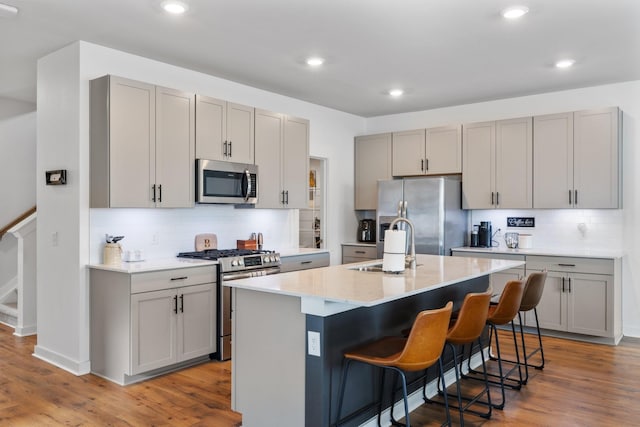 kitchen with gray cabinetry, stainless steel appliances, hardwood / wood-style flooring, and an island with sink