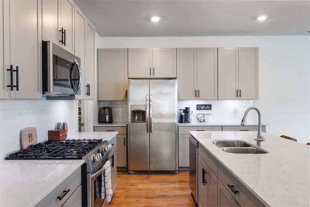 kitchen featuring light stone countertops, sink, stainless steel appliances, decorative backsplash, and light wood-type flooring