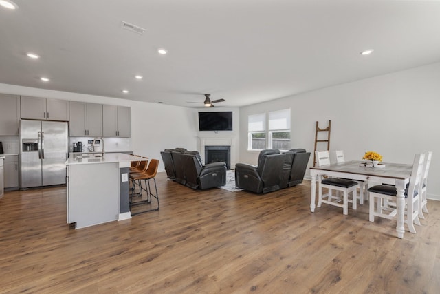 kitchen with ceiling fan, stainless steel fridge, a kitchen bar, gray cabinets, and a center island with sink