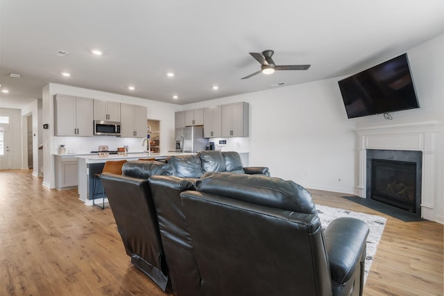 living room with light hardwood / wood-style floors, ceiling fan, and sink