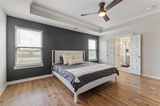 bedroom featuring ensuite bathroom, hardwood / wood-style flooring, ceiling fan, ornamental molding, and a tray ceiling