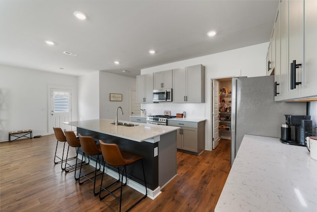 kitchen featuring a center island with sink, a kitchen breakfast bar, sink, dark hardwood / wood-style floors, and appliances with stainless steel finishes