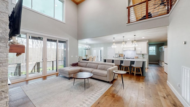 living room featuring a high ceiling, light hardwood / wood-style floors, a healthy amount of sunlight, and a notable chandelier