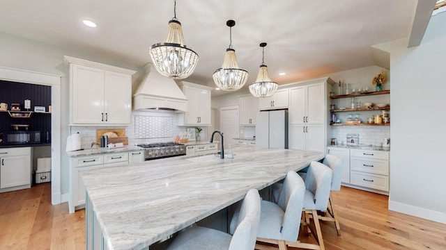 kitchen with a notable chandelier, premium range hood, white fridge, decorative light fixtures, and white cabinets