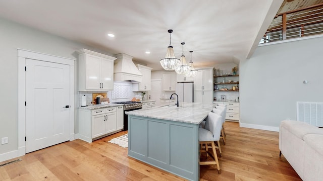 kitchen featuring custom exhaust hood, stainless steel range, decorative light fixtures, white fridge, and white cabinetry