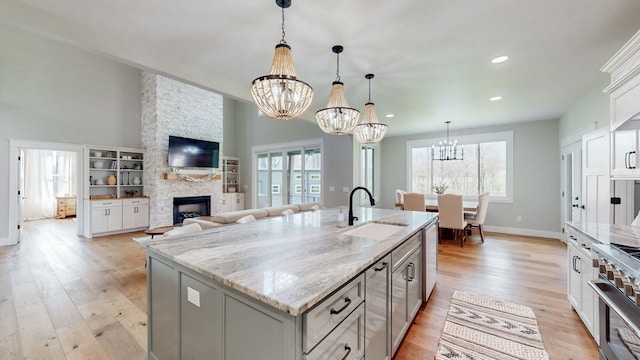 kitchen featuring light stone counters, sink, pendant lighting, a center island with sink, and a stone fireplace