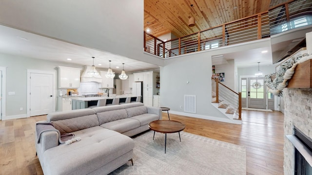 living room featuring a towering ceiling, an inviting chandelier, wooden ceiling, a fireplace, and light hardwood / wood-style floors