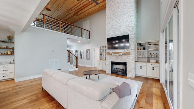 living room with a high ceiling, light hardwood / wood-style flooring, a stone fireplace, and wood ceiling