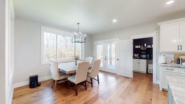 dining space with a notable chandelier, light wood-type flooring, and french doors