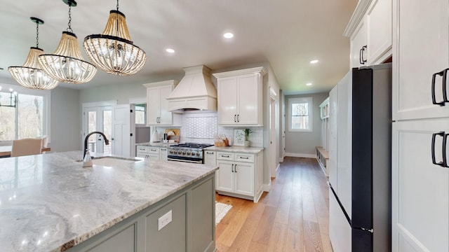 kitchen with white cabinets, sink, premium range hood, and a chandelier