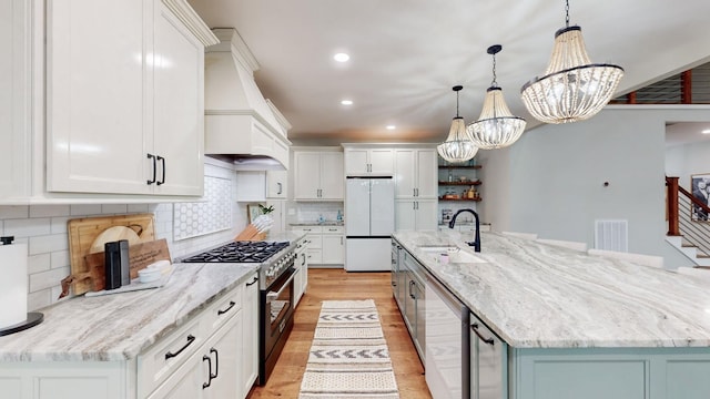 kitchen featuring appliances with stainless steel finishes, a large island with sink, a notable chandelier, white cabinetry, and hanging light fixtures