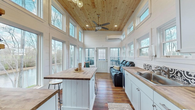 kitchen featuring butcher block counters, sink, wooden ceiling, a high ceiling, and white cabinets