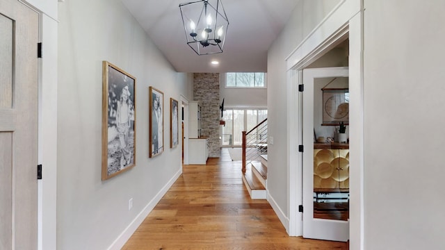 hallway with an inviting chandelier and light wood-type flooring