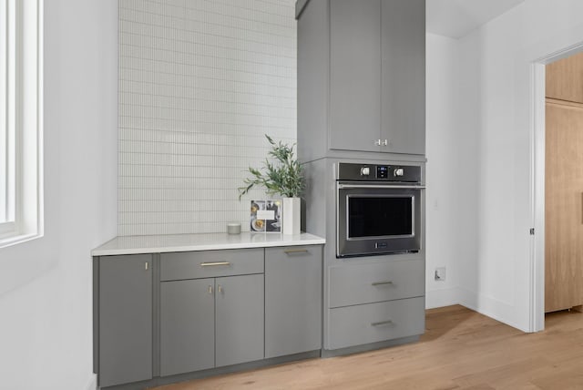 kitchen featuring gray cabinets, stainless steel oven, and light hardwood / wood-style floors