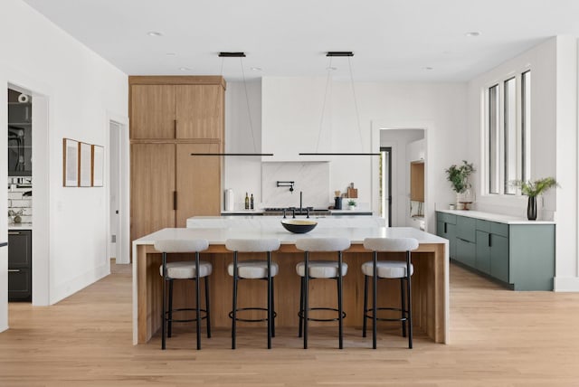 kitchen with pendant lighting, light hardwood / wood-style flooring, a breakfast bar, a kitchen island with sink, and green cabinetry