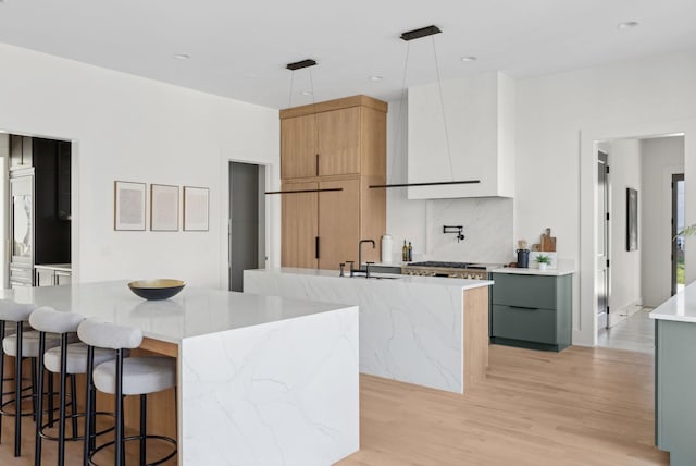 kitchen with white cabinetry, a kitchen island with sink, pendant lighting, and light stone counters