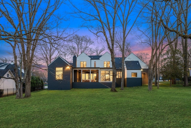 back house at dusk with a sunroom and a lawn