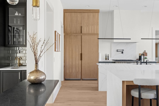 kitchen with wall chimney exhaust hood, sink, light hardwood / wood-style floors, and decorative backsplash